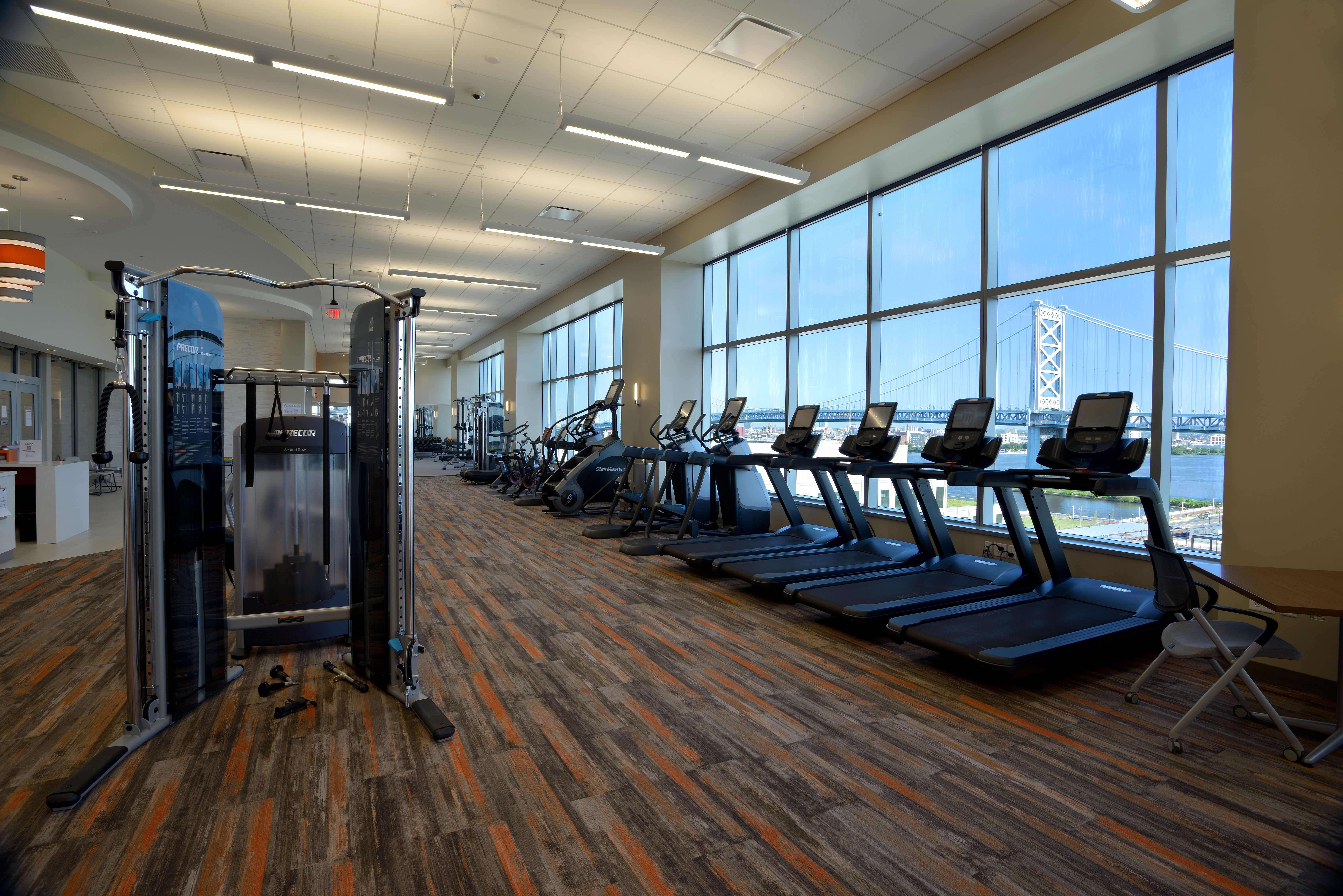 Spacious corporate gym with treadmills and weight station facing river bridge views