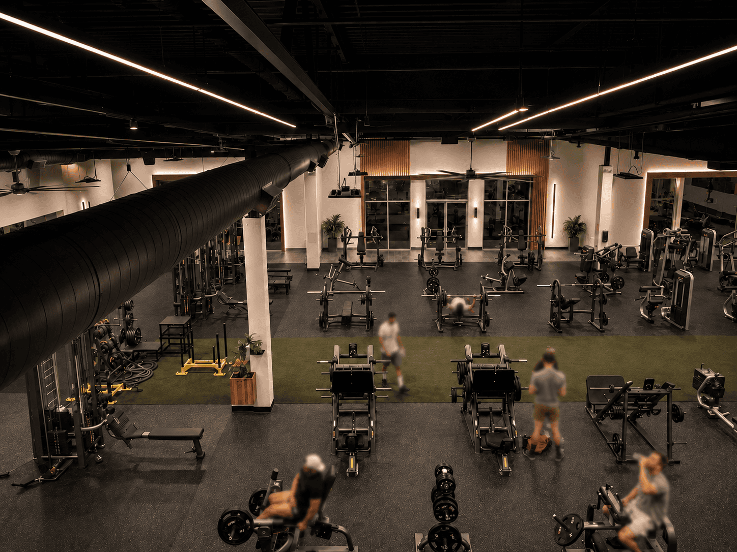 Dark aesthetic gym workout floor with black color scheme, wood-accent wall, and rows of strength machines.