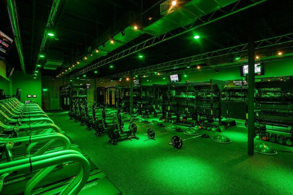 Regymen gym floor with treadmills, weights, and cardio equipment lit in green lighting.