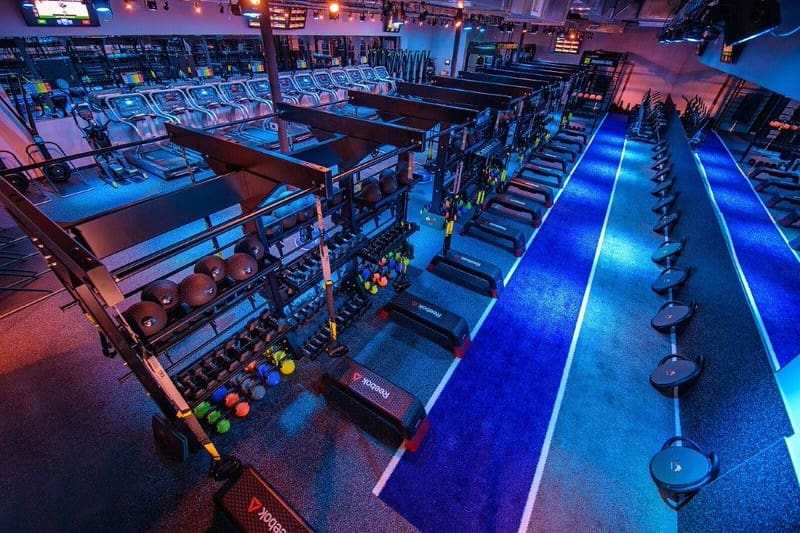 Colorfully lit equipment area at Regymen Fitness with treadmills, strength equipment, and indoor turf training lanes