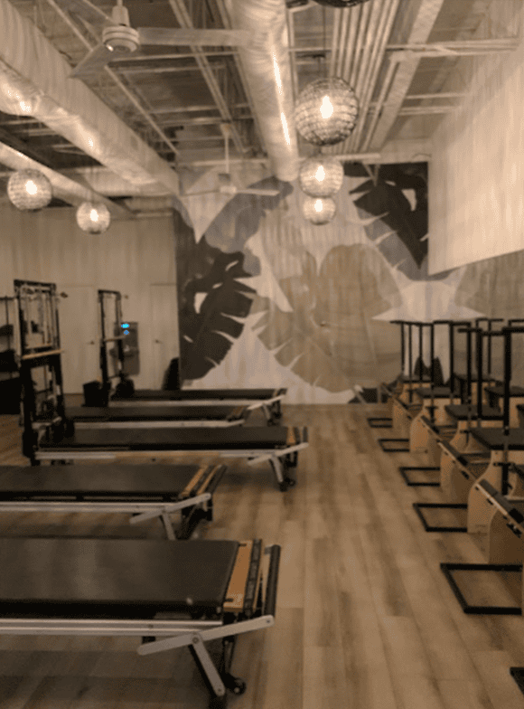 Pilates room design of Longfellow Lumina Studio after renovation with updated earth-tone flooring and ambient lighting.