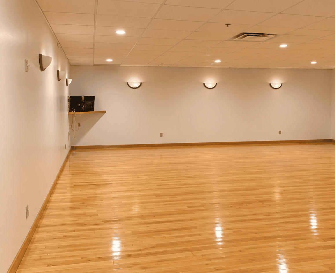 Barre room design of Longfellow Lumina Studio before renovation with wood flooring, neutral walls, and wall-mounted lighting.