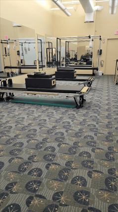Pilates room of Longfellow Lumina Studio in Wayland before renovation with reformers, mirrors, and carpeted floor